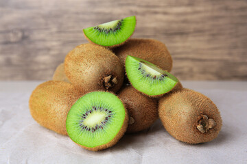 Heap of whole and cut fresh kiwis on parchment paper near wooden wall