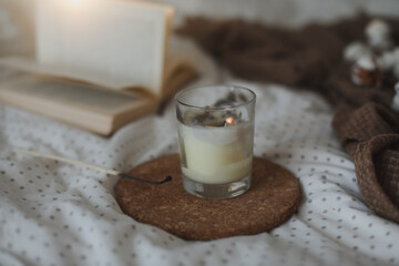 Cozy still life interior details with a book, candle and a cotton twig in warm soft bed. Sweet home