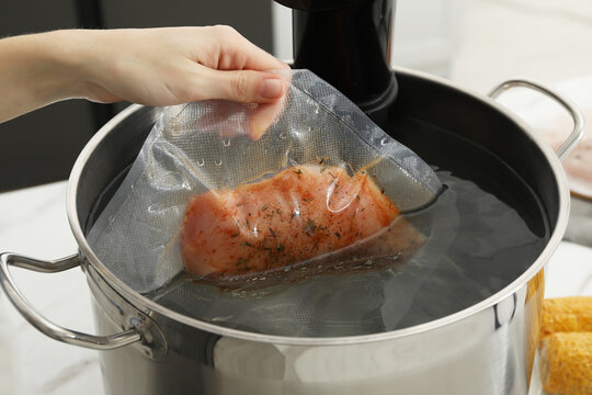 Woman putting vacuum packed meat into pot with sous vide cooker, closeup. Thermal immersion circulator