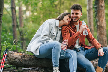 A girl is holding her head on his boyfriend's shoulder and smiling, talking about something witty while sitting at a branch during their nature exploration.