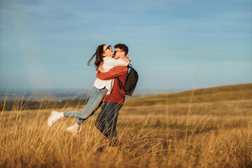 A couple is chatting and hiking in big golden yellow meadow on a sunny autumn day. They wear...