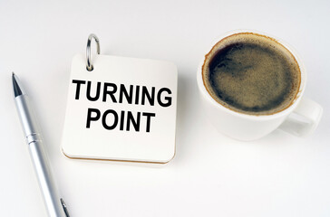 On a white surface, a cup of coffee, a pen and a notepad with the inscription - TURNING POINT