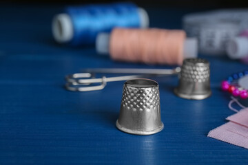 Silver thimble on blue wooden table, space for text. Sewing accessory