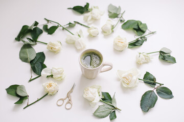 A cup of matcha tea and roses on white background. Flatlay, top view