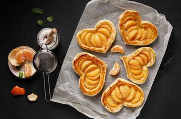 Puff pastry cake in the shape of a heart with tangerine slices on a dark table. top view, copy space