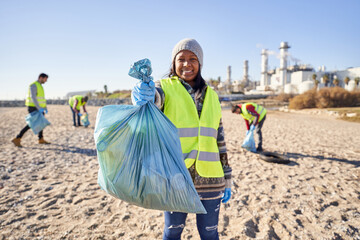 Young latin activist looking at camera holding a garbage bag trash. Group of cleanup volunteers cleaning up waste in nature on sunny day. Concept of environmental protection.