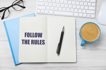 Notebook with phrase Follow The Rules, pen, computer keyboard and cup of coffee on white wooden...