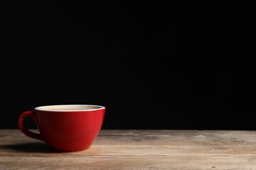 Red ceramic cup with hot aromatic coffee on wooden table against black background, space for text
