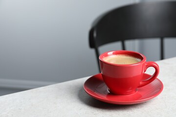 Red ceramic cup with hot aromatic coffee on white table indoors, space for text