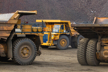 Fototapeta na wymiar Large yellow dump trucks engaged in the transportation of rock mass in the quarry for mining. Machinery and equipment for iron ore mining