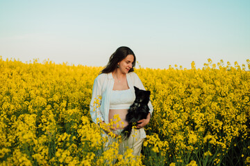 Fototapeta premium A pregnant woman with a small black dog in nature. Rapeseed field