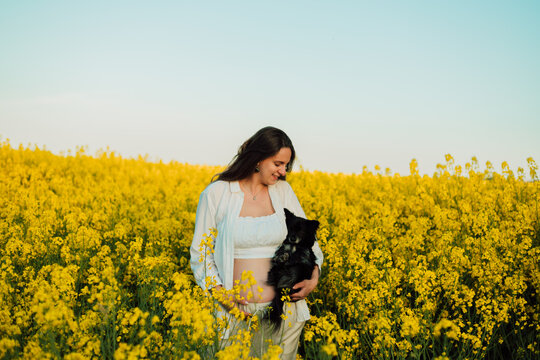 A pregnant woman with a small black dog in nature. Rapeseed field