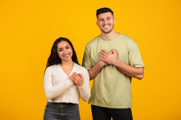 Smiling millennial arab guy and woman in casual clothes press their hands to chest, say thanks