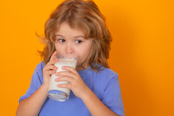 Organic milk. Beautiful smiling child with a glass of milk. Cute boy in blue shirt holding glass of milk on yellow isolated studio background. Portrait of funny kid with milk mustache.