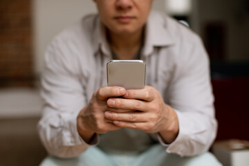 Mature asian man using smartphone, browsing internet or chatting online, selective focus on hands with cellphone