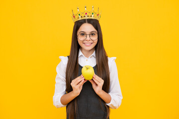 Teen child in queen crown hold apple isolated on yellow background. Princess girl in tiara. Teenage girl wear diadem. Happy girl face, positive and smiling emotions.