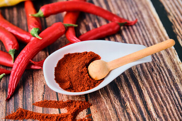 Chili powder and paprika powder in a white spoon on a wooden background with red hot chilli peppers, asian mexican and spanish food condiment