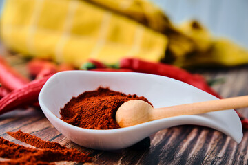 Chili powder and paprika powder in a white spoon on a wooden background with red hot chilli peppers, asian mexican and spanish food condiment