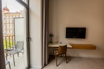 flat tv screen on wall near workspace with chair and balcony in hotel room.