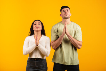 Serious concentrated millennial arab husband and wife folded hands in supplication, make wish, pray