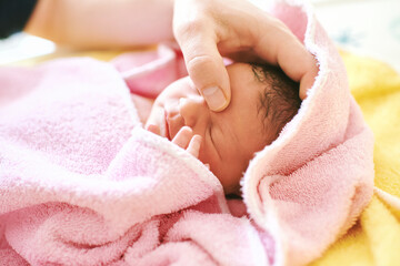 Newborn baby covered in towel after taking bath, father trying to calm down baby with head massage - 561929299