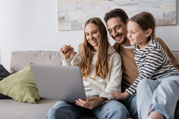 happy family smiling while looking at laptop in living room.
