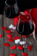 Saint Valentine's Day celebration. Wineglasses with red wine, hearts, gift box, postcard on dark wooden background. Happy holiday . Table decor for festive dinner, romantic atmosphere