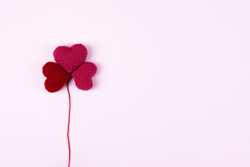 Red crocheted hearts are laid out in the shape of a flower clover on a lilac background. Happy Valentine's Day, Mother's Day and birthday greeting card.
