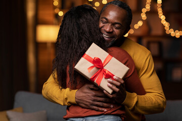 Thankful black man with birthday gift hugging wife at home