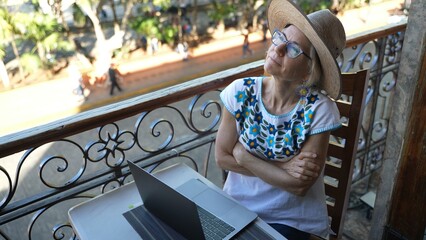 Looking down on a pretty happy mature woman wearing straw hat using a laptop computer pausing to...