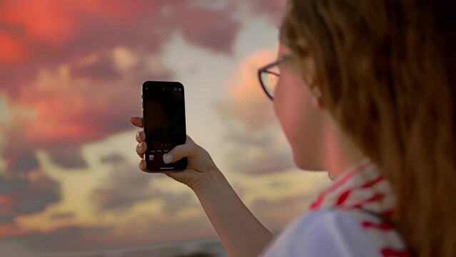 Young european women girl by the sea, takes a selfie and photographs the sunset.