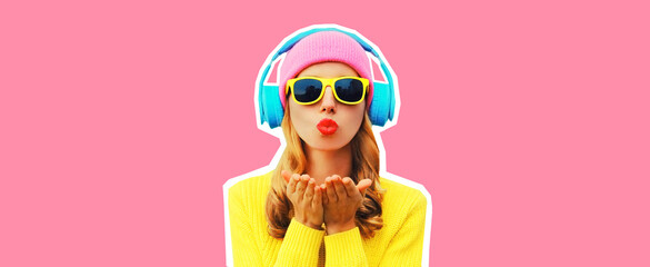 Portrait of stylish young woman in headphones listening to music blowing her lips sends sweet air kiss wearing colorful yellow sweater on pink background