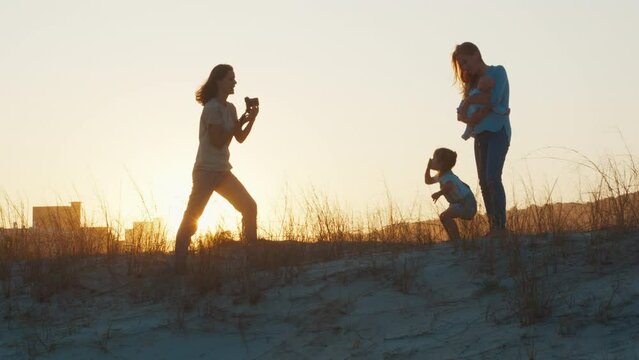 Family photographer. Woman with camera takes picture of the mother with kids at sunset. Family with kids on outdoor photoset on the urban background