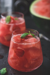 Glass of cool watermelon and strawberry cocktail with fresh mint leaves on dark concrete background