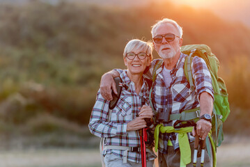 Portrait of an cheerful active senior Caucasian couple hiking in the mountains with backpacks and...