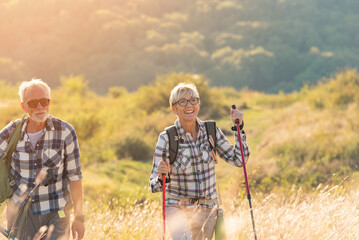 Active senior Caucasian couple hiking in mountains with backpacks and hiking poles, enjoying their adventure