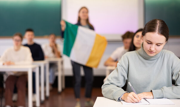 High school teacher tells students about Ireland and holds a Ireland flag in her hands.