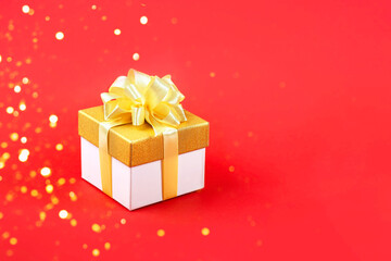 Golden gift box with a satin ribbon bow on red background for a holiday. Happy Valentine's Day, Mother's Day and birthday greeting card.