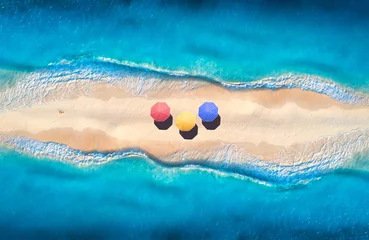 Poster Aerial view of transparent blue sea with waves on the both sides and sandy beach with colorful umbrellas at sunset. Top view of sandbank. Summer travel. Tropical landscape with white sand and ocean © den-belitsky