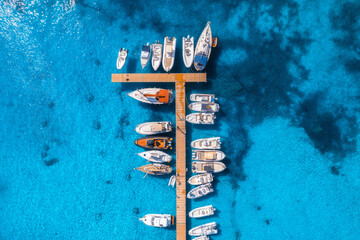 Aerial view of boats and luxury yachts in dock at sunset in summer in Sardinia, Italy. Colorful landscape with sailboats and motorboats in sea bay, jetty, clear blue sea. Top view of harbor. Travel - obrazy, fototapety, plakaty