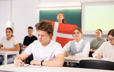 High school teacher tells students about Denmark and holds a Denmark flag in her hands.