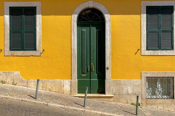 Obraz na płótnie Canvas Traditional and vintage Portuguese house style, Green wooden louver windows and door, Yellow painted cement concrete wall, Slope hilly terrain in city center, Lisbon is capital city of Portugal.