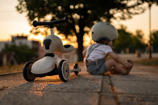 One girl small caucasian toddler child fall of the children's kick scooter wear protective helmet while playing outdoor in summer evening real people leisure growing up concept copy space
