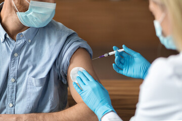 Female Nurse Making Vaccine Injection Shot To Young Male Patient