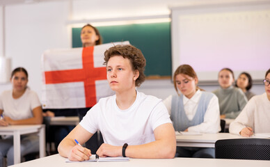 Students study in classroom, teacher stands behind with flag of England