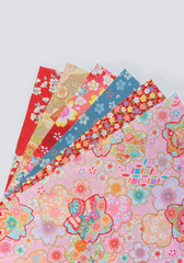 Photograph of a stack of spread-out traditional Japanese furoshiki fabrics decorated with a range of floral patterns designs such as cherry, plum, cosmos or peony blossoms on a white background.