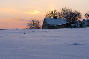 Zimowy zachód słońca nad gospodarstwem wśród zaśnieżonych pól , na szczycie pagórka .