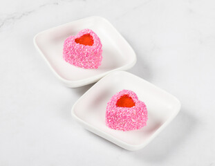 Light delicate dessert without baking. Two small Strawberry cream mousse cakes with jelly filling, in the shape of a heart, sprinkled with pink coconut chips. On a serving plate. White background