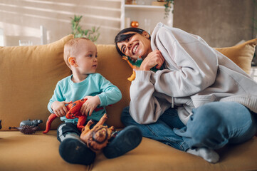 Mother and toddler son playing with dinosaurs toys at home on the couch