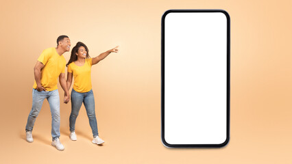 Wow, cool offer. Excited young black couple walking and pointing at giant cellphone with blank...